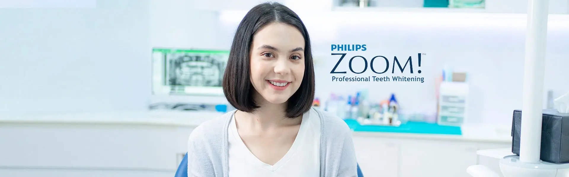 Smiling woman sits in a dental clinic, with "Philips Zoom! Professional Teeth Whitening" text beside her. The setting is clean and modern.